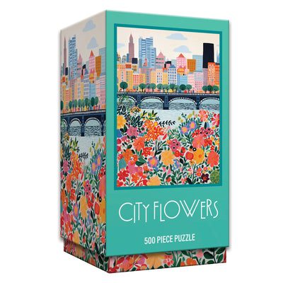 The ROSEART Vertical Visions City Flowers 500 piece jigsaw puzzle showcases vibrant city buildings, a bridge, and colorful flowers in the foreground.