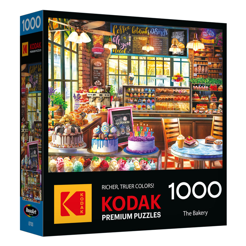 The image shows the ROSEART - KODAK PREMIUM - THE BAKERY 1000 piece jigsaw puzzle box, featuring a vibrant scene of cakes, pastries, and desserts on display.