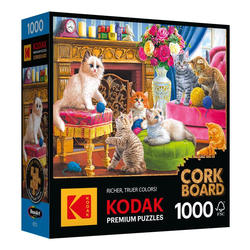 A box containing the 1000-piece RoseArt Kodak Cork jigsaw puzzle titled "Kittens by the Fireplace," which features an image of playful kittens lounging in a lavish, colorfully decorated room.
