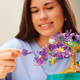 The patient artisan assembles a Crystal Gem Creations Blossoming Bonsai, adorned with purple flowers. Each delicate piece added enhances the miniature into an enchanting work of art.