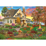 This vibrant ROSEART - KODAK PREMIUM CORK- LAKESIDE HOME 1000-piece jigsaw puzzle captures a colorful home with a wraparound porch, fire pit, and bicycle, surrounded by flowers and trees. A serene lake and sunset sky complete the picturesque setting reminiscent of a Kodak moment.