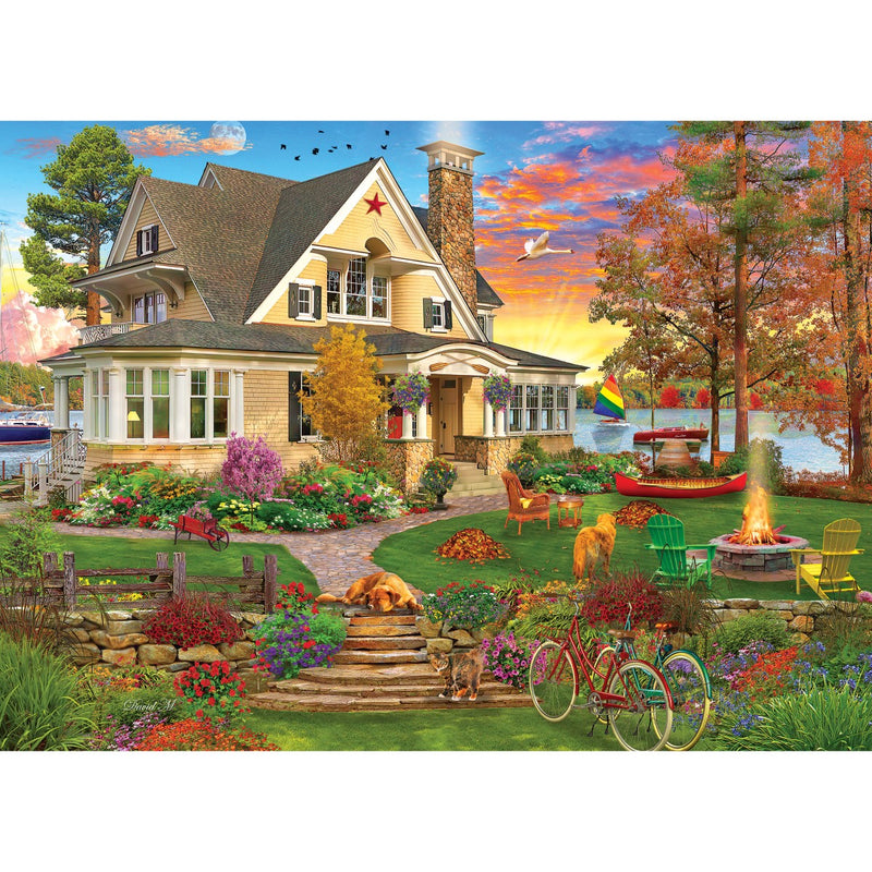 A delightful scene depicted in the Cra-Z-Art - RoseArt - Kodak Cork - Lakeside Home 1000 Piece Jigsaw Puzzle features a vibrant lakeside home nestled among autumn trees and blooming flowers, complete with a charming garden. Chairs surround a cozy fire pit, with a bicycle resting nearby and a picturesque sailboat drifting peacefully on the lake.