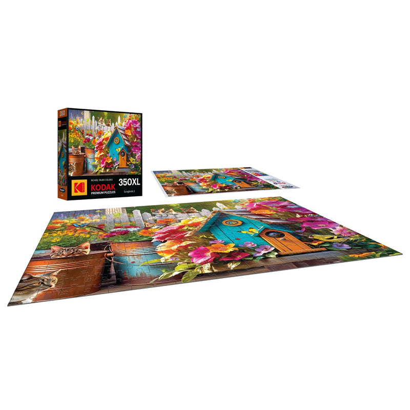 A 350-piece jigsaw puzzle from RoseArt's Kodak Premium collection, titled "Songbirds 2," features a vivid birdhouse scene adorned with colorful flowers and charming songbirds. The partially assembled image highlights the beauty of nature, while the puzzle box for "Songbirds 2" is also in view.