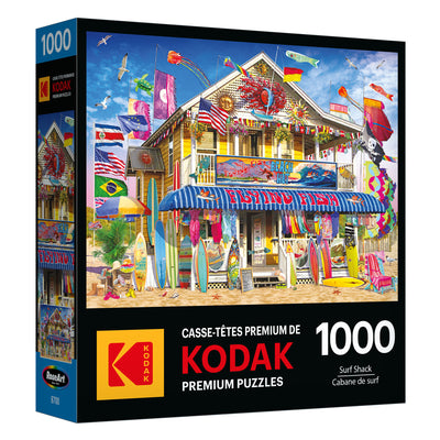 The ROSEART KODAK PREMIUM 1000-piece jigsaw puzzle box features a vibrant surf shack scene with surfboards, kites, and flags—ideal for enthusiasts.