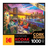 Box of RoseArt - Kodak Cork - Manhattan Balcony Sunset - 1000 Piece Jigsaw Puzzle showing a 1000-piece jigsaw puzzle with an image of a sunset cityscape including a bridge and outdoor seating area.