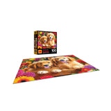 A completed ROSEART - KODAK PREMIUM - GOLDEN PUPPY PALS - 100 PIECE JIGSAW PUZZLE featuring two golden puppies among flowers sits next to its box, both showcasing the adorable pups in a vibrant floral setting.