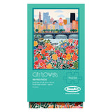 The ROSEART - VERTICAL VISIONS - CITY FLOWERS 500 piece jigsaw puzzle showcases a vibrant cityscape with illustrated buildings, a bridge, and blooming flowers in the foreground.