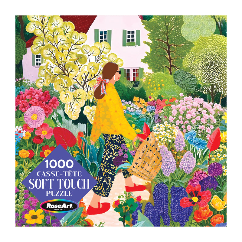 A woman with long brown hair walks through a vibrant garden in front of a white house on the ROSEART Soft Touch Picking Flowers 1000 piece jigsaw puzzle box.