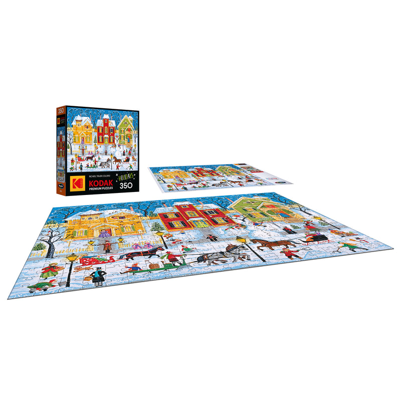 A completed ROSEART KODAK PREMIUM "After the Snow Falls" 350 piece jigsaw puzzle and its box, both showcasing a vibrant winter village scene with people, houses, and snow.