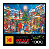 A festive holiday scene of people in winter clothes by a decorated Christmas tree in a charming village; ROSEART - KODAK PREMIUM - CHRISTMAS VILLAGE - 1000 PIECE JIGSAW PUZZLE.