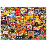 The ROSEART KODAK CORK ANTIQUE SIGNS 1000-piece jigsaw puzzle features a collage of vintage product signs, including soda, dyes, bread, and medicines, set against a grassy background with autumn leaves for a nostalgic touch.