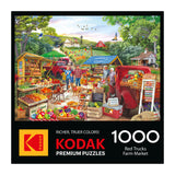 The ROSEART KODAK PREMIUM RED TRUCKS FARM MARKET 1000 Piece Jigsaw Puzzle box shows a vibrant rural farm market with red trucks, produce stands, and shoppers. Text highlights the product name and piece count.