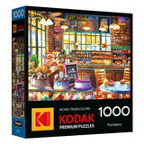 The image shows the ROSEART - KODAK PREMIUM - THE BAKERY 1000 piece jigsaw puzzle box, featuring a vibrant scene of cakes, pastries, and desserts on display.