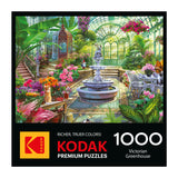 Enjoy the ROSEART - KODAK PREMIUM Victorian Greenhouse 1000 Piece Jigsaw Puzzle, featuring a lush greenhouse scene with a fountain, tropical plants, flowers, and white furniture.