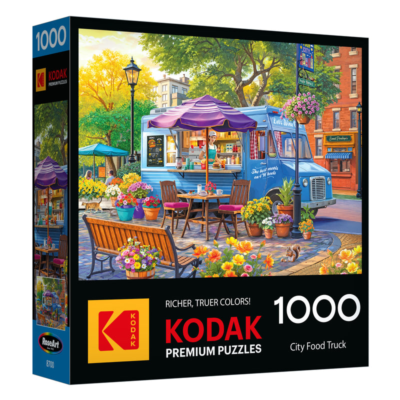 The ROSEART-KODAK PREMIUM CITY FOOD TRUCK 1000-piece jigsaw puzzle features an illustrated city scene with food trucks, outdoor seating, flowers, and colorful buildings in the background.
