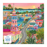 The ROSEART-MILLIE ILLUSTRATES-CHARLESTON-300 PIECE JIGSAW PUZZLE features a colorful illustrated cityscape of Charleston with churches, historic buildings, gardens, cars on winding roads, and a river with boats at sunset.