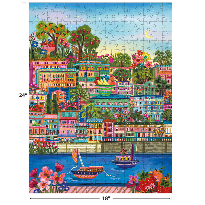 The ROSEART-MILLIE ILLUSTRATES-PORT DE SOLLER 300 Piece Jigsaw Puzzle features a vibrant coastal town with buildings, greenery, flowers, and boats on blue water. Finished size: 24" x 18".