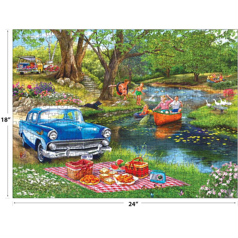 The ROSEART-BIGELOW ILLUSTRATIONS-GOOD TIMES AT THE RIVER 500-piece jigsaw puzzle (18"x24") features a vintage blue car by a picnic blanket, people canoeing, kids swimming, and lush green park scenery.