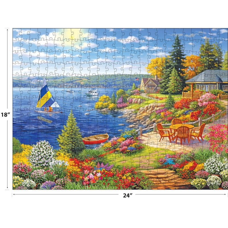 The ROSEART-KODAK PREMIUM-LAKESHORE LIVING 350 piece jigsaw puzzle (18x24 in) features a colorful lakeside garden, patio set, sailboats, charming houses and trees under a bright blue sky.