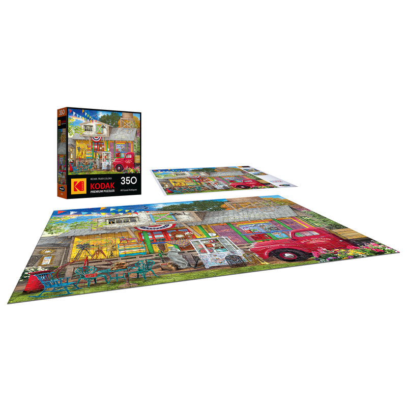 The ROSEART-KODAK PREMIUM All Good Antiques 350-piece jigsaw puzzle showcases a lively antique shop scene with a red vintage truck, outdoor chairs, and delightful decorations.