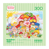 The ROSEART-STRAWBERRY SHORTCAKE-BERRY BESTIES 300 piece jigsaw puzzle features colorful cartoon characters and animals in front of a big strawberry house, surrounded by greenery and flowers.
