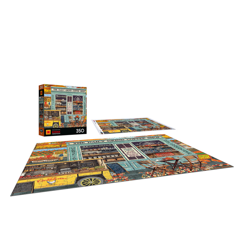 The ROSEART-KODAK PREMIUM THE DAILY GRIND 350-piece jigsaw puzzle is shown assembled on a surface, with its box and a vibrant storefront scene reference image placed nearby.