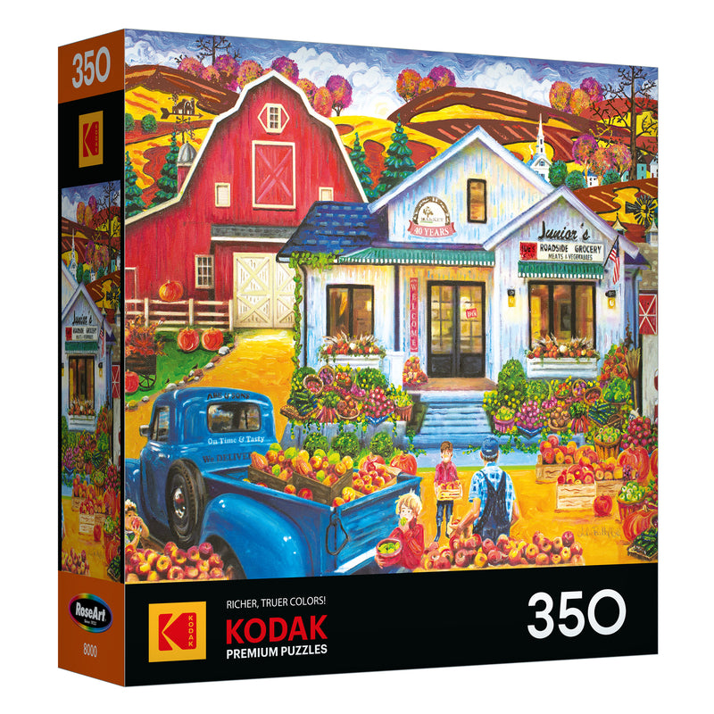 The ROSEART-KODAK PREMIUM Junior's Farmer's Market 350-piece jigsaw puzzle features a vibrant fall farm stand scene with apples, a red barn, blue truck, people, and colorful autumn scenery.