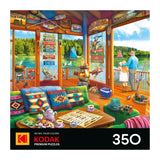Colorful lake house cabin with ROSEART-KODAK PREMIUM-THE LAKE HOUSE-350 PIECE JIGSAW PUZZLE and tea on the table, overlooking a lake where a man and girl fish from the porch as sailboats pass by.