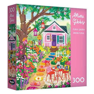 The ROSEART-OLIVIA GIBBS-FLORAL GARDEN-300 PIECE JIGSAW PUZZLE features a vibrant illustration of a pink house, outdoor table and chairs, and colorful flowers in a lively garden scene.