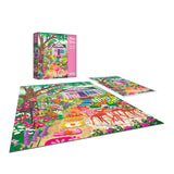 The ROSEART-OLIVIA GIBBS-FLORAL GARDEN 300-piece jigsaw puzzle features a vibrant floral garden with flowers, trees, a pink house, and outdoor furniture; puzzle box is shown in the background.