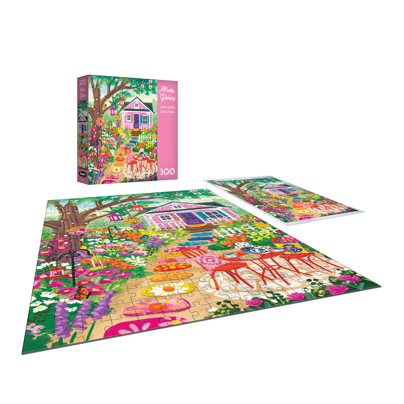 The ROSEART-OLIVIA GIBBS-FLORAL GARDEN 300-piece jigsaw puzzle features a vibrant floral garden with flowers, trees, a pink house, and outdoor furniture; puzzle box is shown in the background.