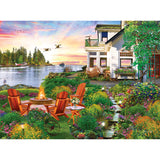 A scenic backyard features a seating area with four wooden chairs around a fire pit, surrounded by vibrant flowers and greenery, overlooking a lake with ducks flying and boats in the water—just like the image on the RoseArt - My Happy Place - Harbor House - 750 Piece Jigsaw Puzzle.