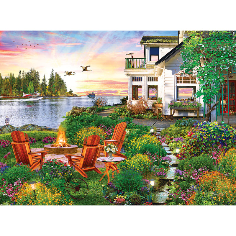 A scenic backyard features a seating area with four wooden chairs around a fire pit, surrounded by vibrant flowers and greenery, overlooking a lake with ducks flying and boats in the water—just like the image on the RoseArt - My Happy Place - Harbor House - 750 Piece Jigsaw Puzzle.