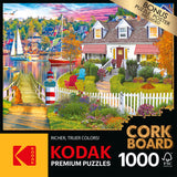 A RoseArt - Kodak Cork - Charles Harbor - 1000 Piece Jigsaw Puzzle box displaying a 1000-piece puzzle of a vibrant lakeside scene with a house, garden, sailboats, and colorful autumn trees. Text highlights "bonus puzzle poster included.