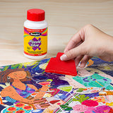 A hand applies RoseArt - 4.5 oz Puzzle Glue 6 pack to a colorful completed puzzle using a red applicator on a light wooden surface.