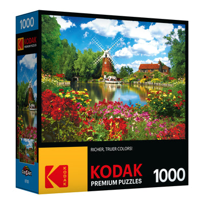 Box of RoseArt - Kodak Premium 1000 Piece Jigsaw Puzzle featuring an image of Hunsett Mill and the River Ant, Norfolk, England with a charming cottage surrounded by vibrant flowers and a waterway.
