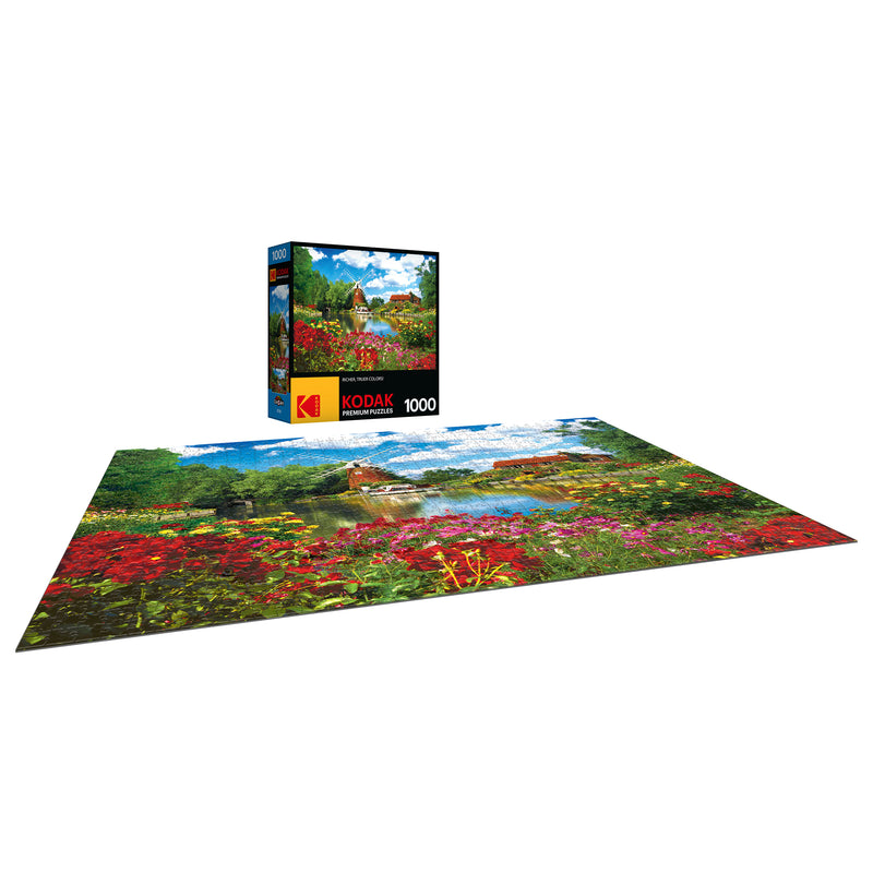 A completed RoseArt - Kodak Premium - Hunsett Mill and the River Ant, Norfolk, England - 1000 Piece Jigsaw Puzzle featuring a colorful garden scene with a small building and trees, shown beside its box with matching image.