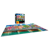 A colorful, completed RoseArt - Kodak Premium - Colorful Waterfront Buildings, Amsterdam - 1000 Piece Jigsaw Puzzle depicting a vibrant city canal scene with buildings. The puzzle box is standing upright in the background, displaying the same image.