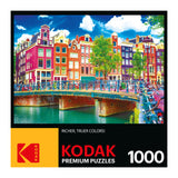 A colorful puzzle box labeled "RoseArt - Kodak Premium - Colorful Waterfront Buildings, Amsterdam - 1000 Piece Jigsaw Puzzle," featuring an image of a vibrant cityscape with multicolored buildings, a canal, and a bridge with bicycles. Text reads "Richer, truer colors!".