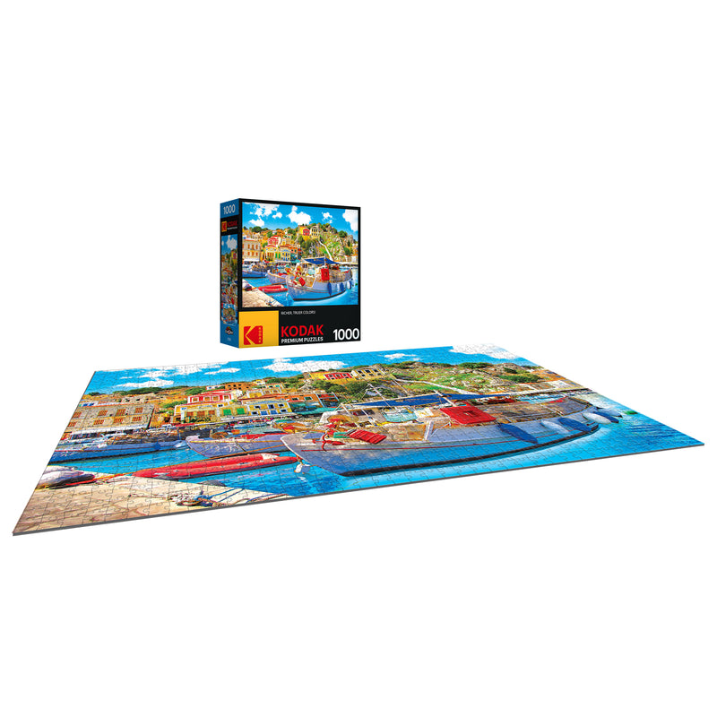 A completed 1000-piece RoseArt - Kodak Premium - Symi with Boats in the Harbor, Greece - 1000 Piece Jigsaw Puzzle depicting a colorful seaside town, with the puzzle box showing the same image in the background.