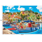 A completed RoseArt - Kodak Premium - Symi with Boats in the Harbor, Greece - 1000 Piece Jigsaw Puzzle depicting a vibrant coastal village with colorful buildings, boats docked at a harbor, and a bright blue sky with fluffy clouds. Puzzle dimensions are 19.25" x 26.625".