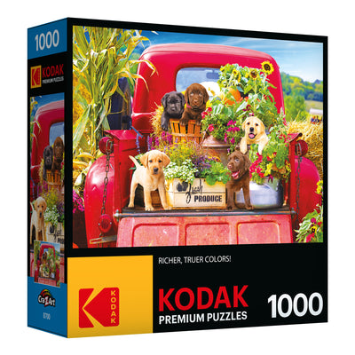 Box of a RoseArt - Kodak Premium - Stowaways - 1000 Piece Jigsaw Puzzle featuring an image of puppies sitting on the back of a red truck with flowers and produce. The puzzle has 1000 pieces and showcases rich, true colors.