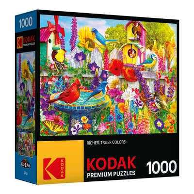 A 1000-piece RoseArt - Kodak Premium - Bird Bath Garden - 1000 Piece Jigsaw Puzzle box featuring a vibrant garden scene with various colorful birds, flowers, and a birdhouse.