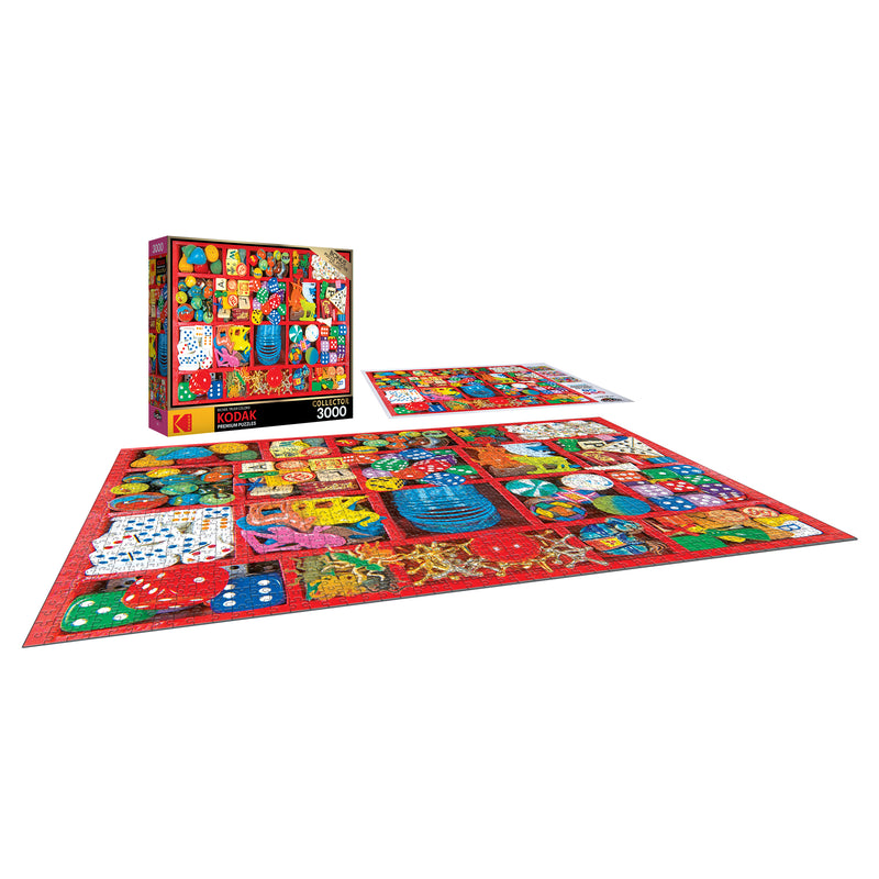 A 3000-piece RoseArt - Kodak Premium - Vintage Toy Box - 3000 Piece Jigsaw Puzzle depicting a colorful, art-themed collage partially assembled on a red backdrop with the puzzle box standing nearby.