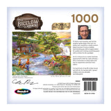 The back of a RoseArt - Chris Bigelow - Fishing from the Banks - 1000 Piece Jigsaw Puzzle box features an illustration of a riverside cabin scene and a brief biography of the artist, Chris Bigelow, including his photograph. The puzzle's dimensions are also listed.