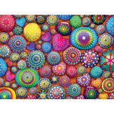 A collection of brightly colored, intricately patterned stones and hearts arranged on an orange surface. The designs feature various geometric shapes and vibrant colors. It's the RoseArt - Kodak Cork - Mandala Stones - 1000 Piece Jigsaw Puzzle.
