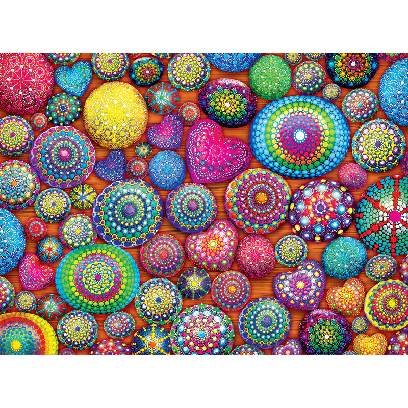A collection of brightly colored, intricately patterned stones and hearts arranged on an orange surface. The designs feature various geometric shapes and vibrant colors. It's the RoseArt - Kodak Cork - Mandala Stones - 1000 Piece Jigsaw Puzzle.