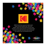 Colorful puzzle pieces on a black background with a central yellow Kodak logo and text promoting RoseArt - Kodak Premium - Village Areopoli - 1000 Piece Jigsaw Puzzle and their quality. RoseArt logo and website are also displayed.