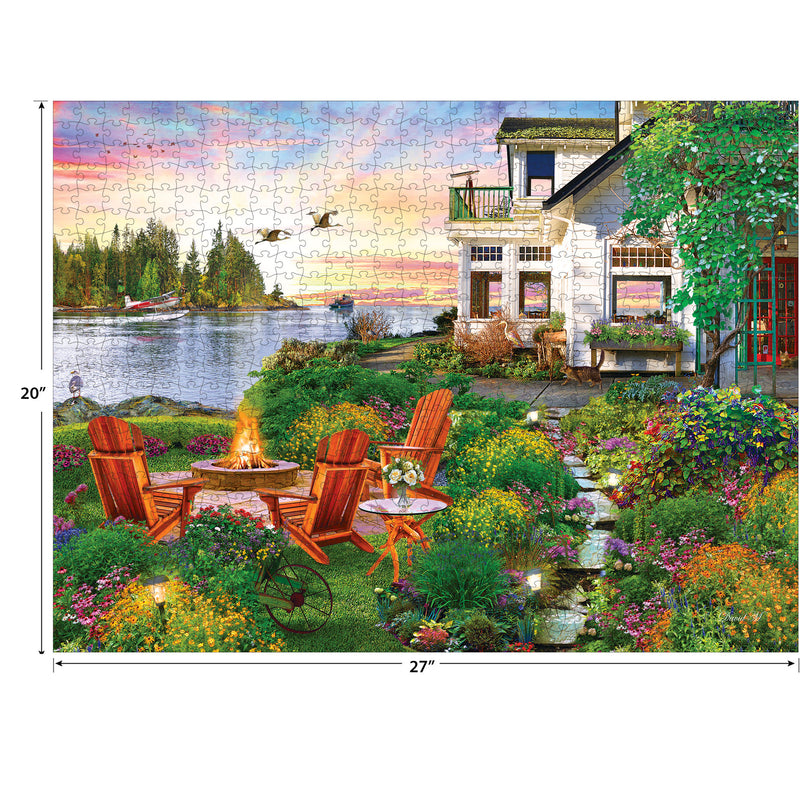A RoseArt - My Happy Place - Harbor House - 750 Piece Jigsaw Puzzle depicting a lakeside garden with a fire pit, Adirondack chairs, a house, and a lake view at sunset. The assembled dimensions are 27 inches by 20 inches.