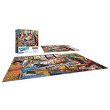A 1000-piece jigsaw puzzle featuring a busy, colorful street shop scene. The puzzle is shown completed on a flat surface with the box standing upright next to it. This is RoseArt - Back to the Past - Record Store - 1000 Piece Jigsaw Puzzle.